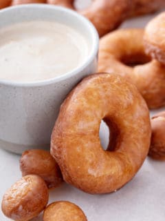 Homemade doughnut resting against the side of a cup of coffee.