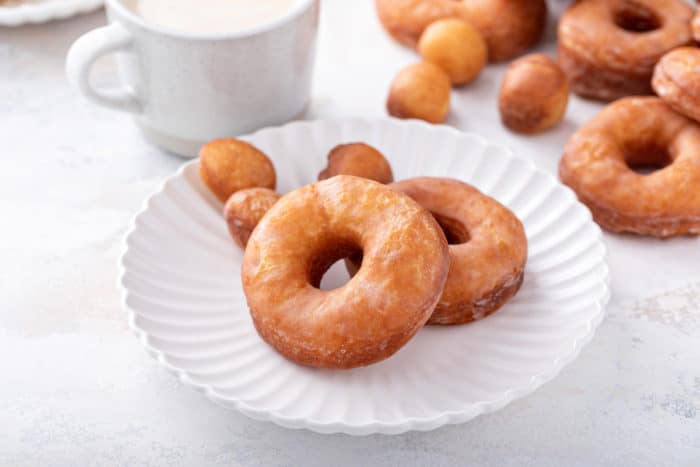 Two homemade doughnuts and three doughnut holes set on a white plate.