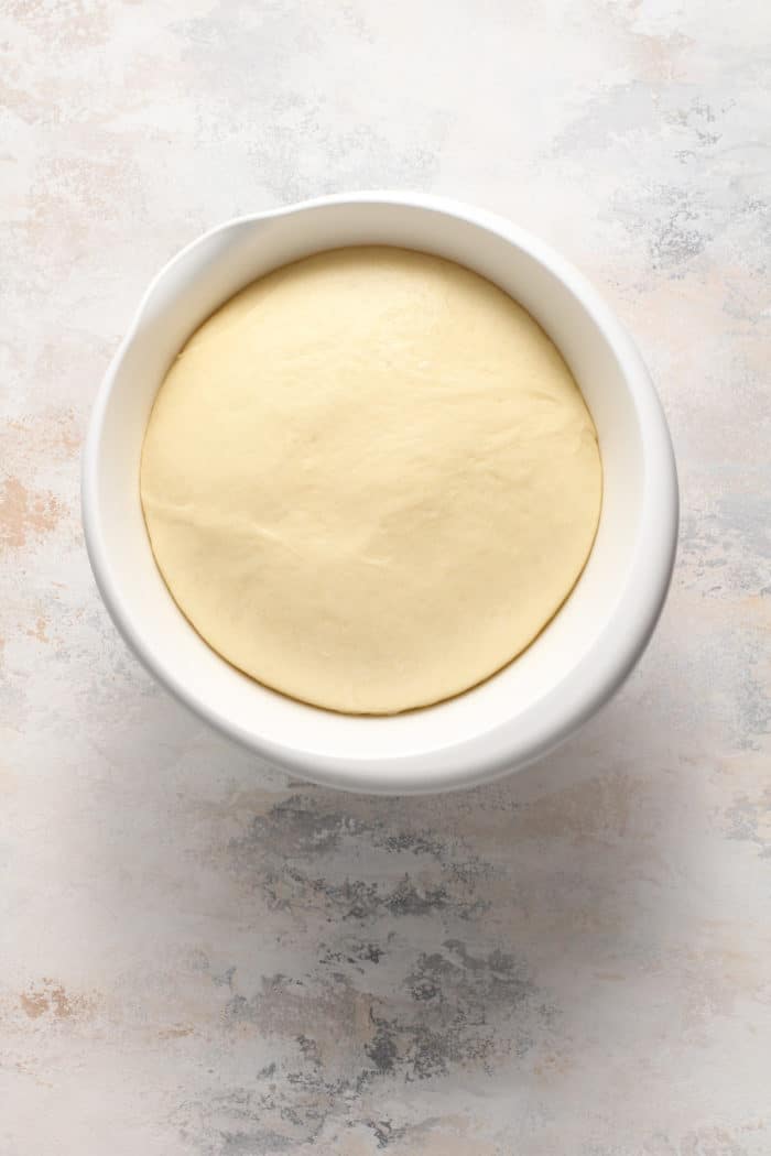 Risen doughnut dough in a white bowl.