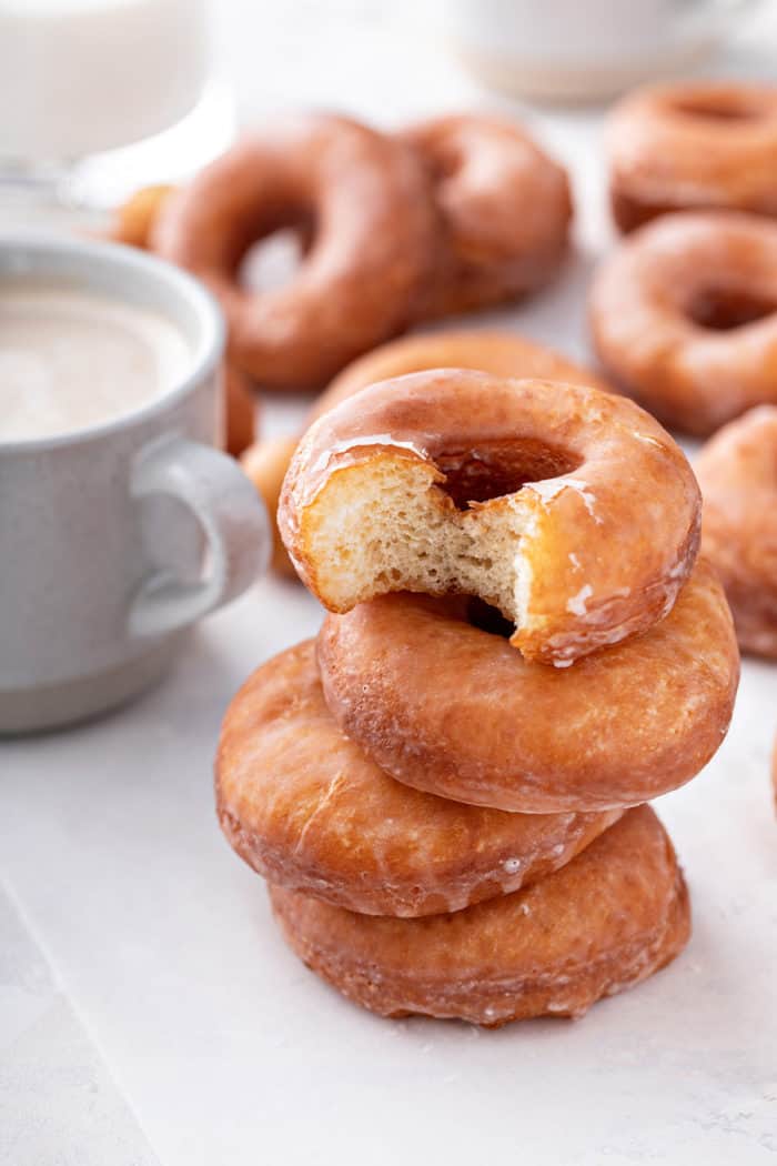 Four stacked homemade doughnuts, with a bite taken out of the top doughnut.