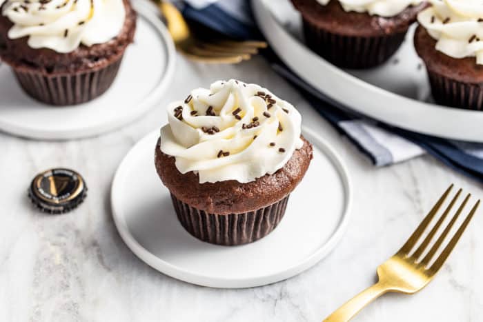 Frosted Guinness cupcake on a white plate with a platter of cupcakes in the background