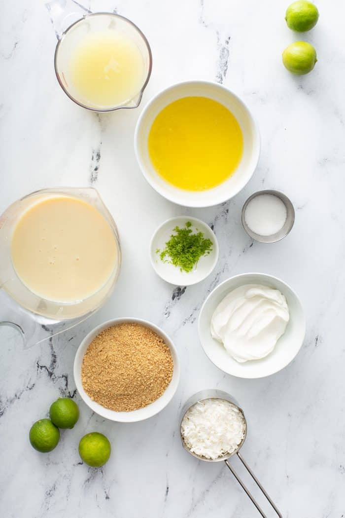 Overhead view of the ingredients for key lime pie bars measured into various bowls on a marble counter