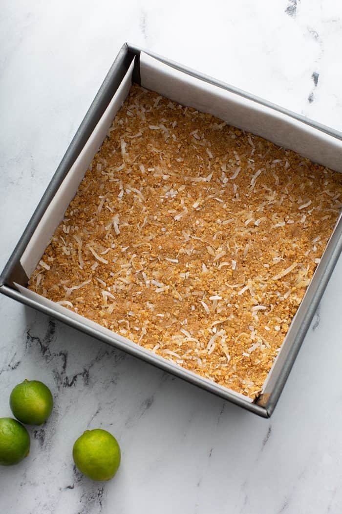 Coconut graham cracker crust in a parchment-lined baking pan on a marble countertop