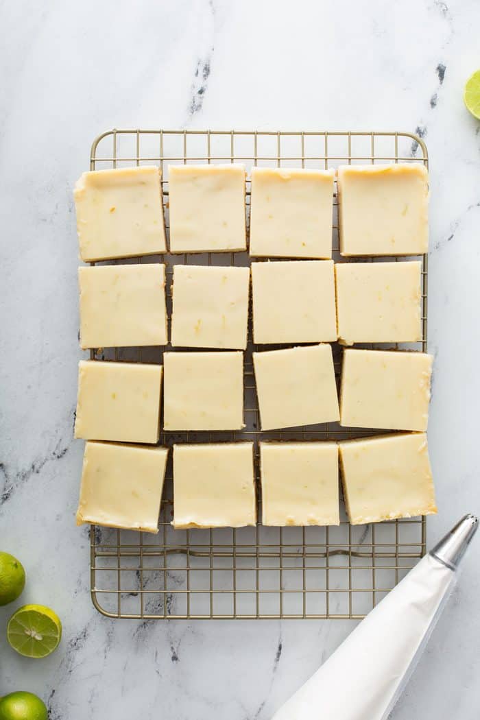 Overhead view of key lime pie bars cut into 16 pieces on a wire rack set on a marble counter