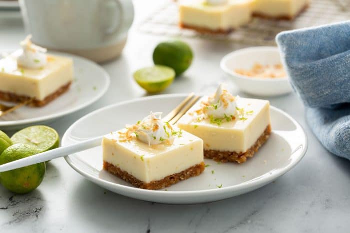 Key lime pie bars on a white plate with another plate of bars and a wire rack with more bars in the background