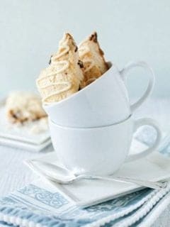 Two cherry white chocolate scones sitting in a white mug stacked on another on a plate with a spoon