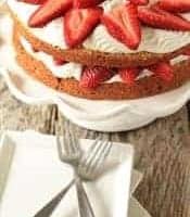 Strawberry cream cake on a cake stand behind a plate with two forks