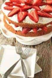 Strawberry cream cake on a cake stand behind a plate with two forks