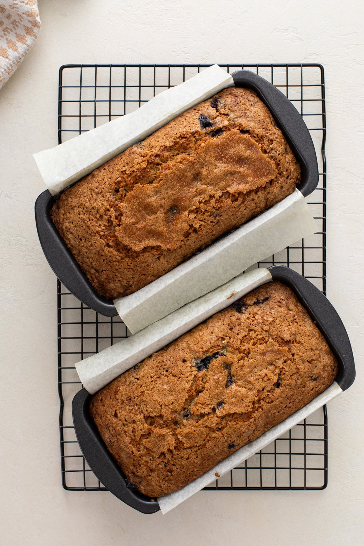 Two loaves of blueberry zucchini bread in parchment-lined pans cooling on a wire rack.