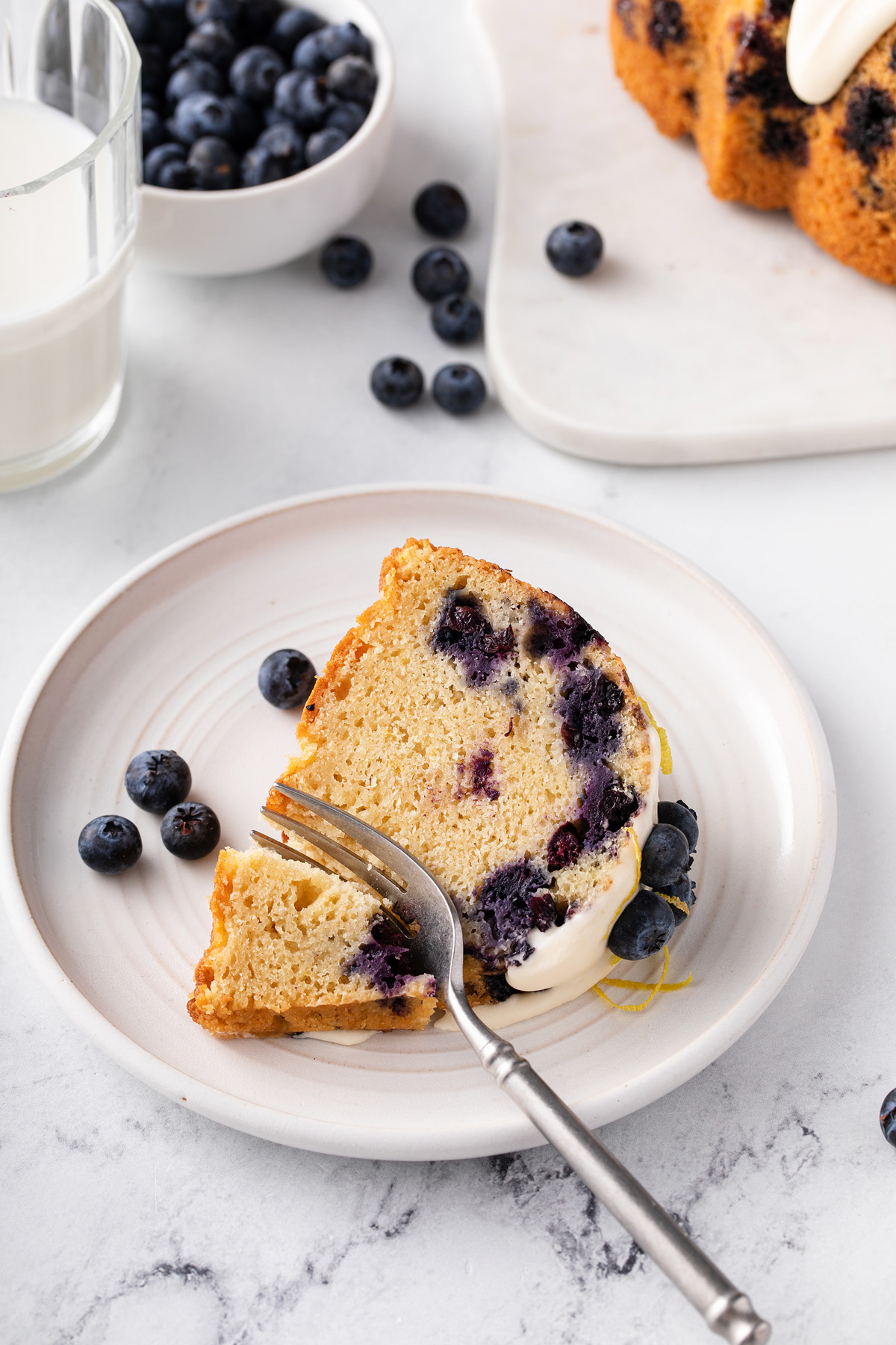 Slice of lemon-blueberry bundt cake being cut into with a fork on a white plate.
