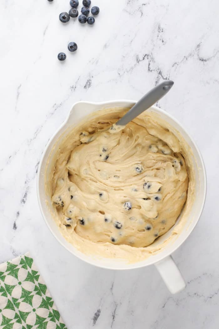 Blueberries folded into the cake batter for lemon-blueberry bundt cake in a white mixing bowl.