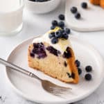 Slice of glazed lemon-blueberry bundt cake on a white plate.