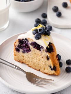 Slice of glazed lemon-blueberry bundt cake on a white plate.