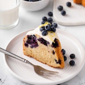 Slice of glazed lemon-blueberry bundt cake on a white plate.