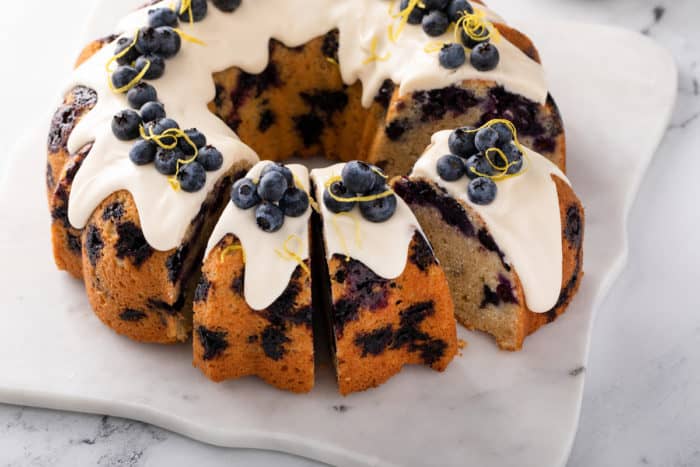 Sliced lemon-cream cheese bundt cake garnished with lemon zest and whole blueberries.