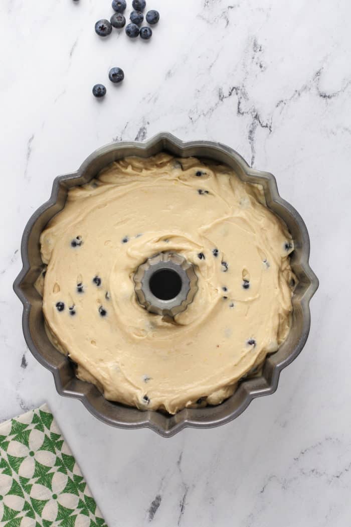 Lemon-blueberry bundt cake batter spread into a bundt pan, ready to go in the oven.