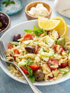 White plate of greek orzo salad garnished with wedges of lemon