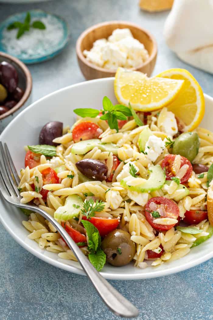 White plate of greek orzo salad garnished with wedges of lemon