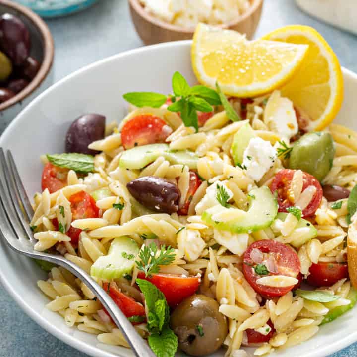 White plate of greek orzo salad garnished with wedges of lemon