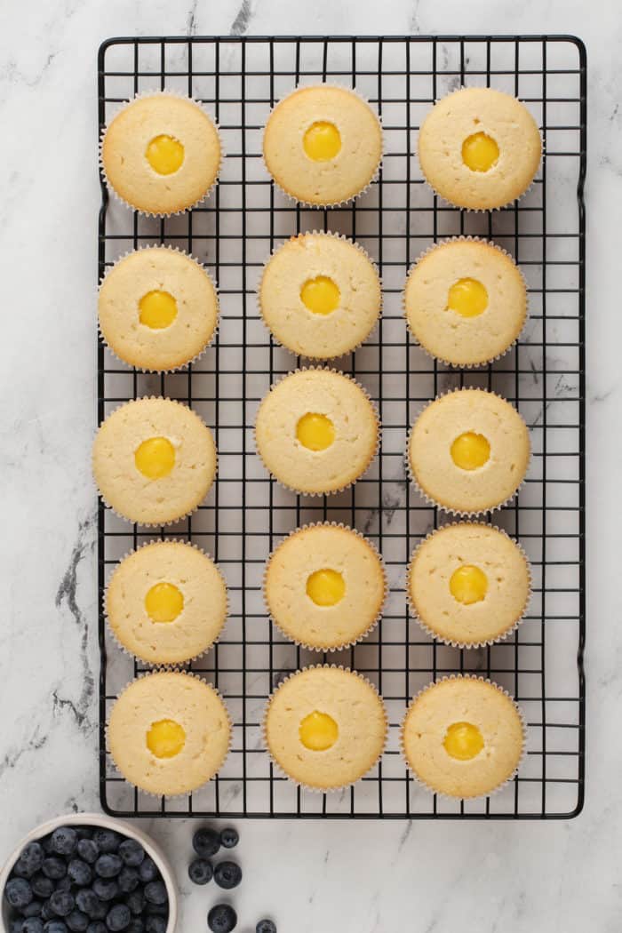 Overhead view of lemon cupcakes filled with lemon curd set on a wire cooling rack.