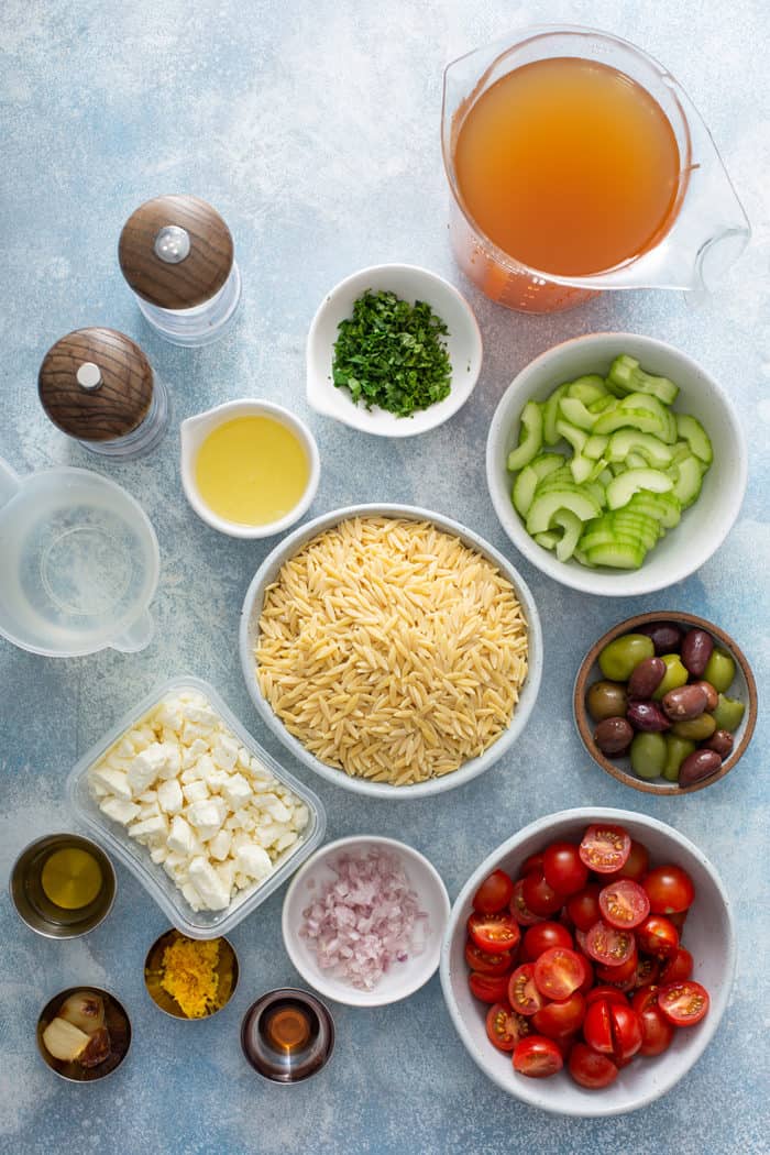 Ingredients for greek orzo salad arranged on a blue countertop