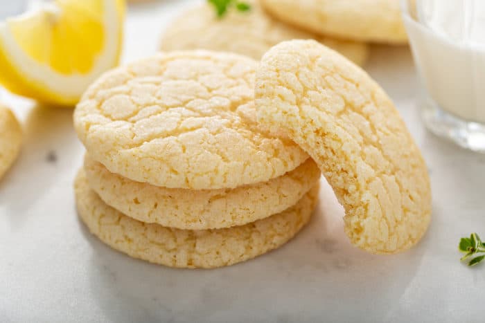 Chewy lemon sugar cookies in a stack. A cookie with a bite out of it is leaning against the stack.