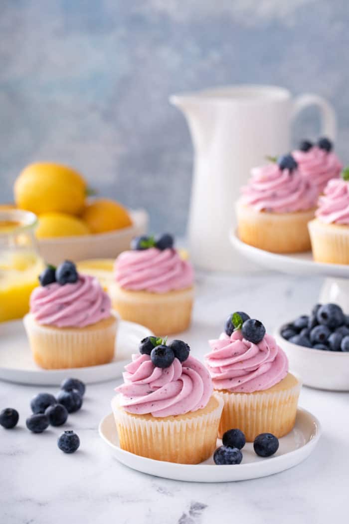 Lemon cupcakes topped with lemon-blueberry frosting on white plates.