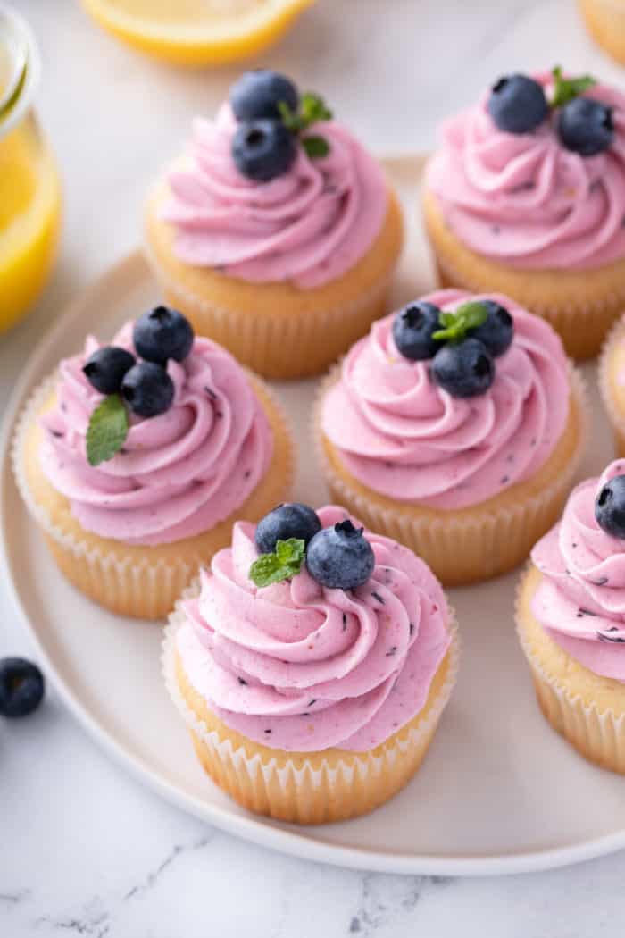 White platter filled with lemon cupcakes topped with lemon-blueberry frosting.