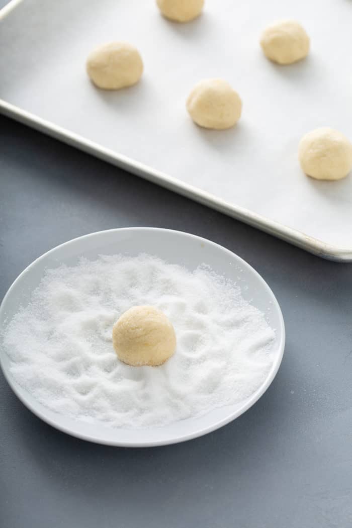 Ball of chewy sugar cookie dough being rolled in granulated sugar