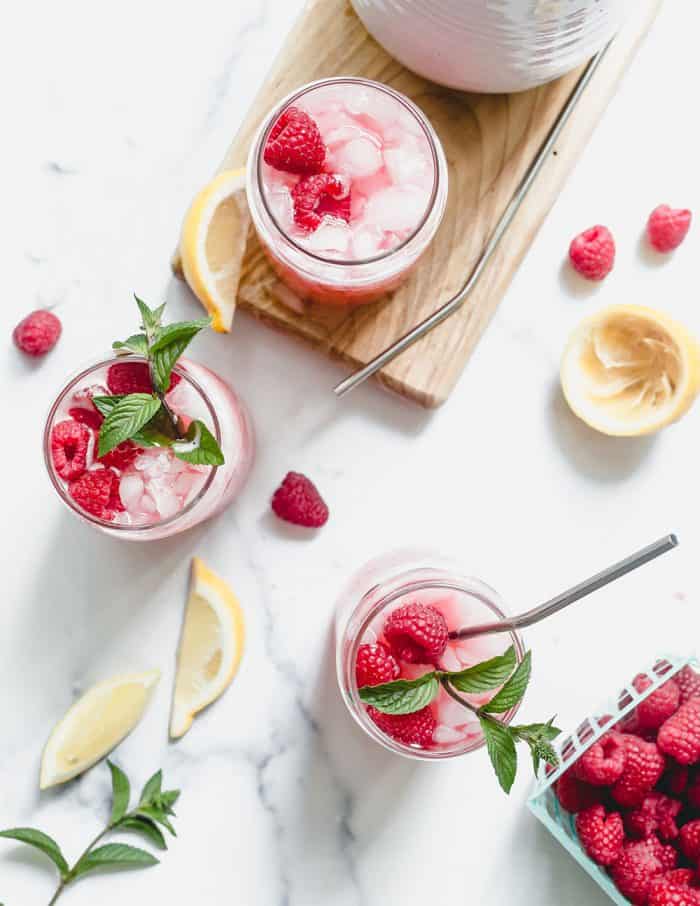 Overhead view of three glasses of raspberry lemonade garnished with mint, surrounded by fresh raspberries and lemon slices