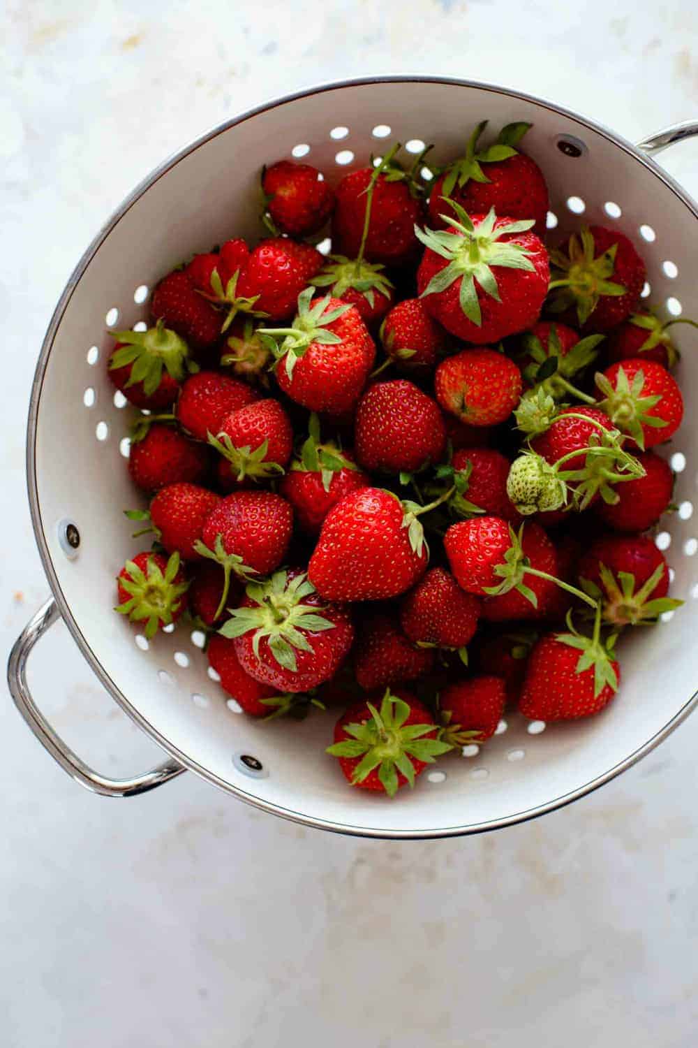 Whole fresh strawberries in a white colander