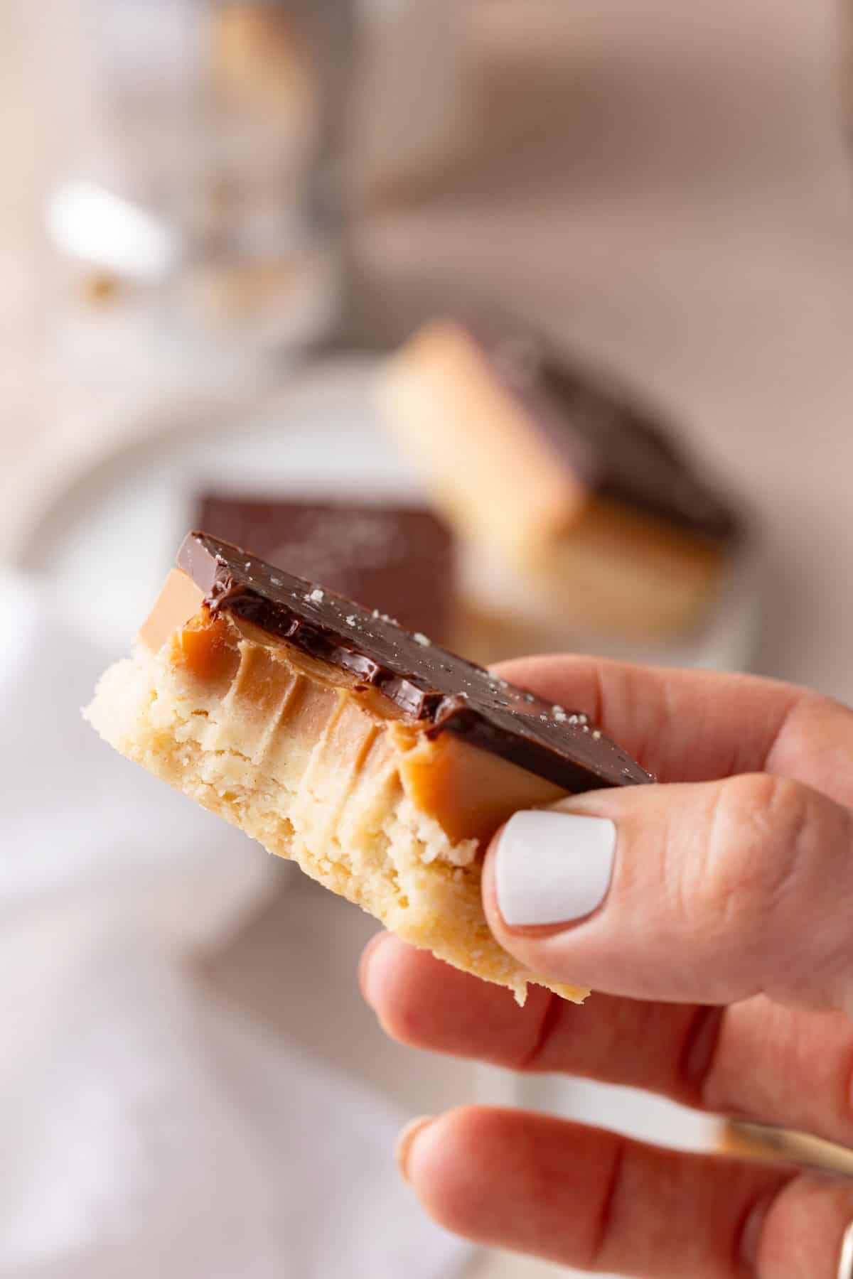 Hand holding up a piece of millionaire shortbread with a bite taken from the corner.