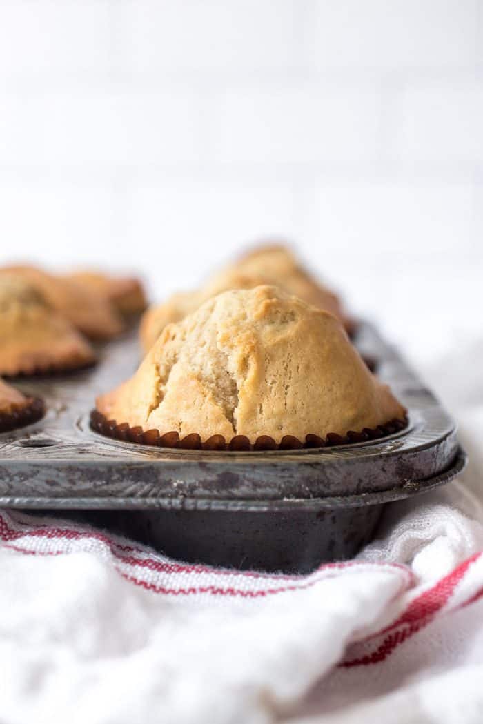 Freshly baked donut muffins in a muffin tin set on a dish towel on a countertop