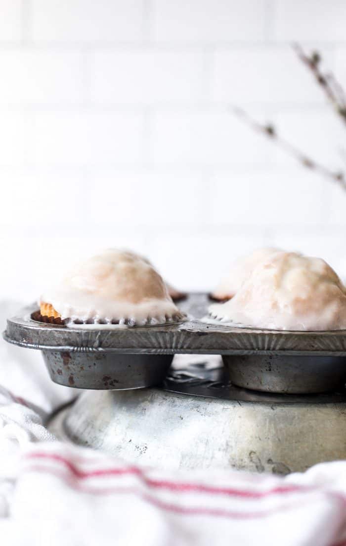 Glazed donut muffins in a muffin tin on a kitchen towel set on a counter