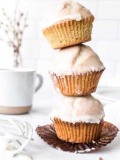 Three glazed donut muffins stacked on top of each other on a white countertop, with a coffee mug in the background