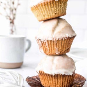 Three glazed donut muffins stacked on top of each other on a white countertop, with a coffee mug in the background