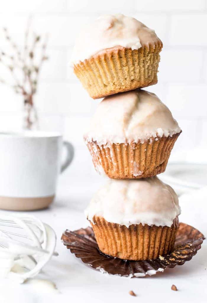 Three glazed donut muffins stacked on top of each other on a white countertop, with a coffee mug in the background