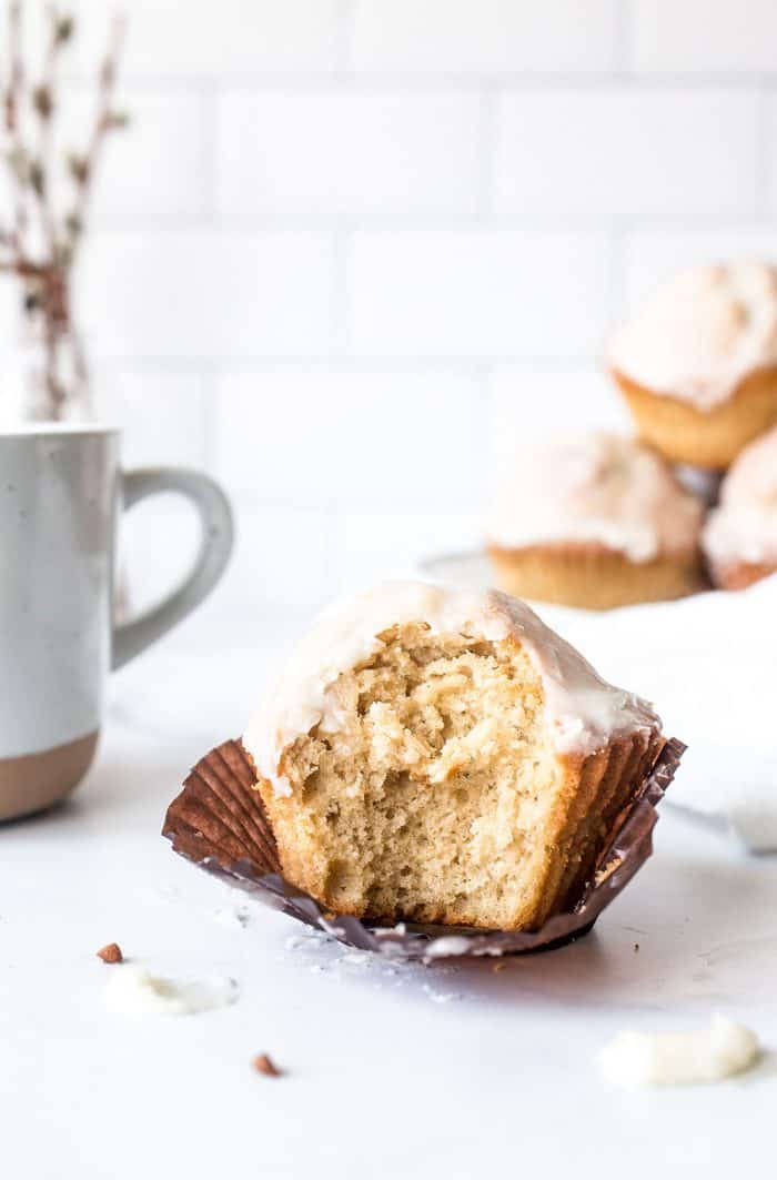 Glazed donut muffin with a bite taken out of it, set on a counter next to a coffee mug