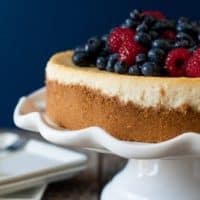 Lemon cheesecake topped with berries on a white cake stand