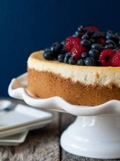 Lemon cheesecake topped with berries on a white cake stand