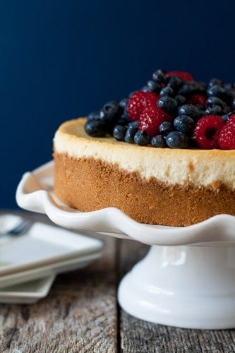 Lemon cheesecake topped with berries on a white cake stand