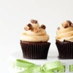 Two snicker cupcakes on a white cake stand with a green ribbon