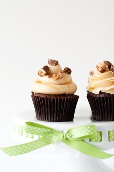 Two snicker cupcakes on a white cake stand with a green ribbon