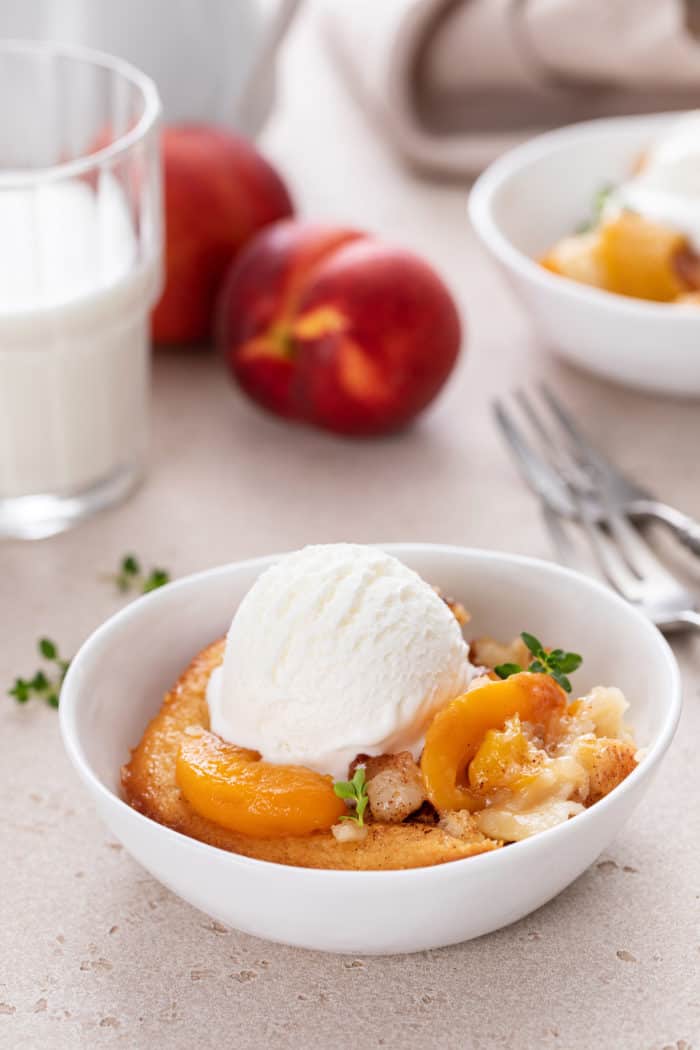 Serving of homemade peach cobbler topped with a scoop of vanilla ice cream in a white bowl.