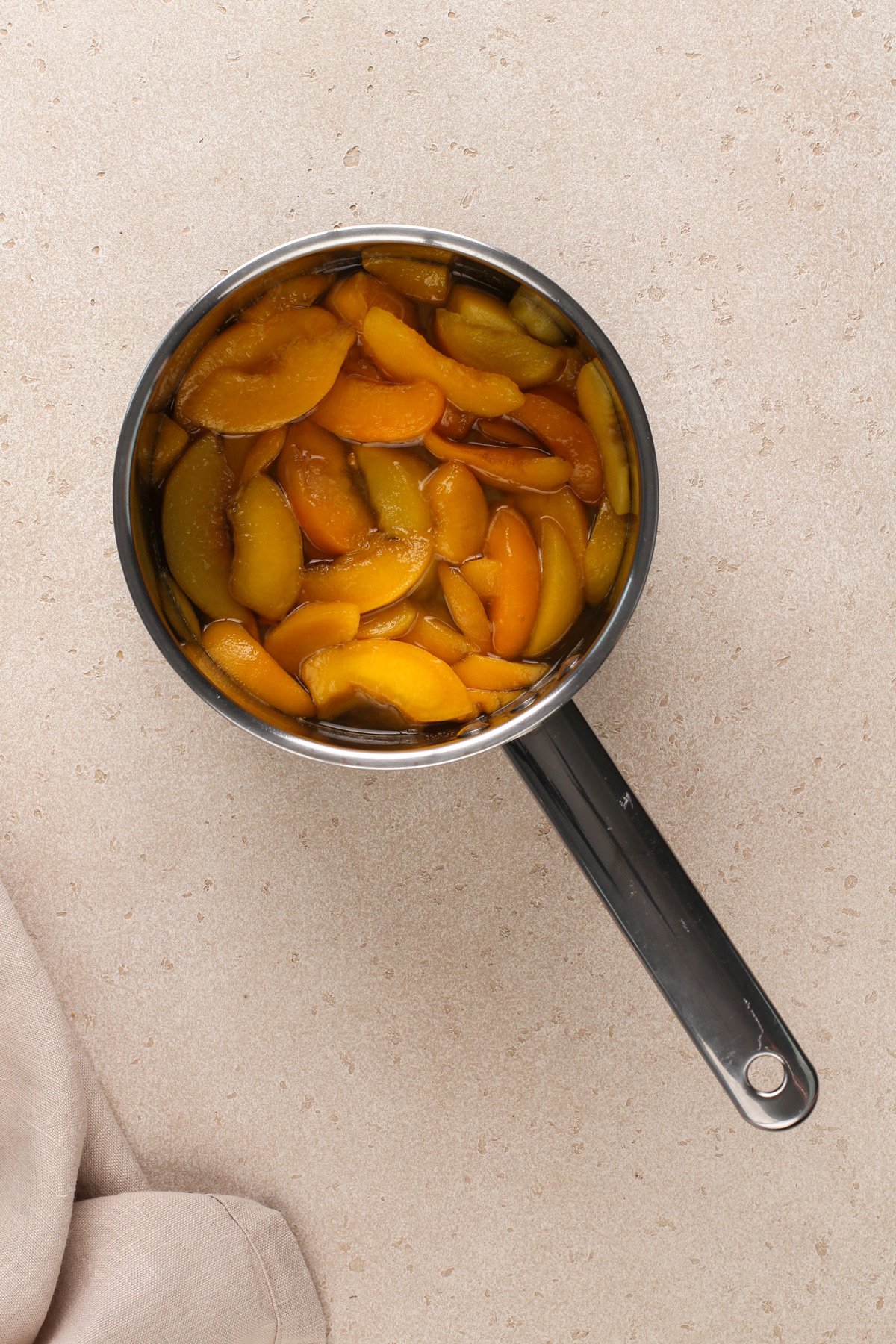 Peaches cooked down in a metal saucepan.