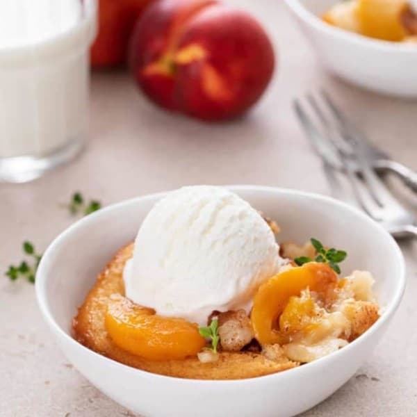 Serving of homemade peach cobbler topped with a scoop of vanilla ice cream in a white bowl.