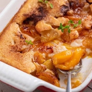 Spoon dishing homemade peach cobbler out of a pan of the cobbler.