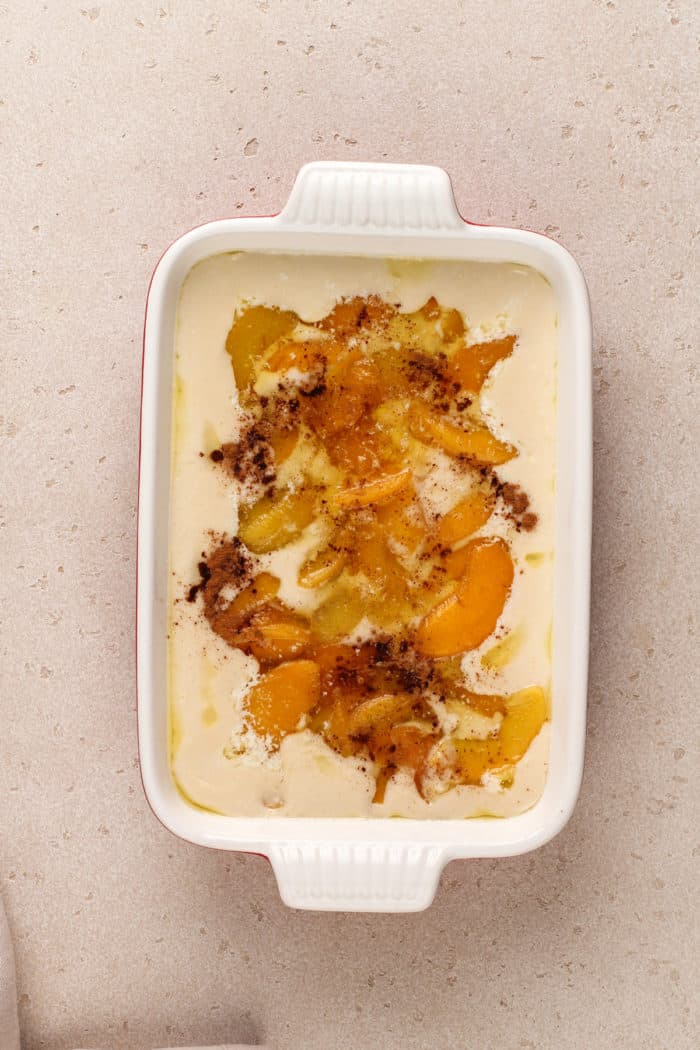 Homemade peach cobbler assembled in a white baking dish, ready to go in the oven.