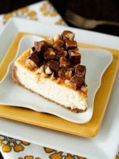 Slice of Snickers cheesecake on a stack of yellow and white plates