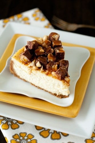 Slice of Snickers cheesecake on a stack of yellow and white plates